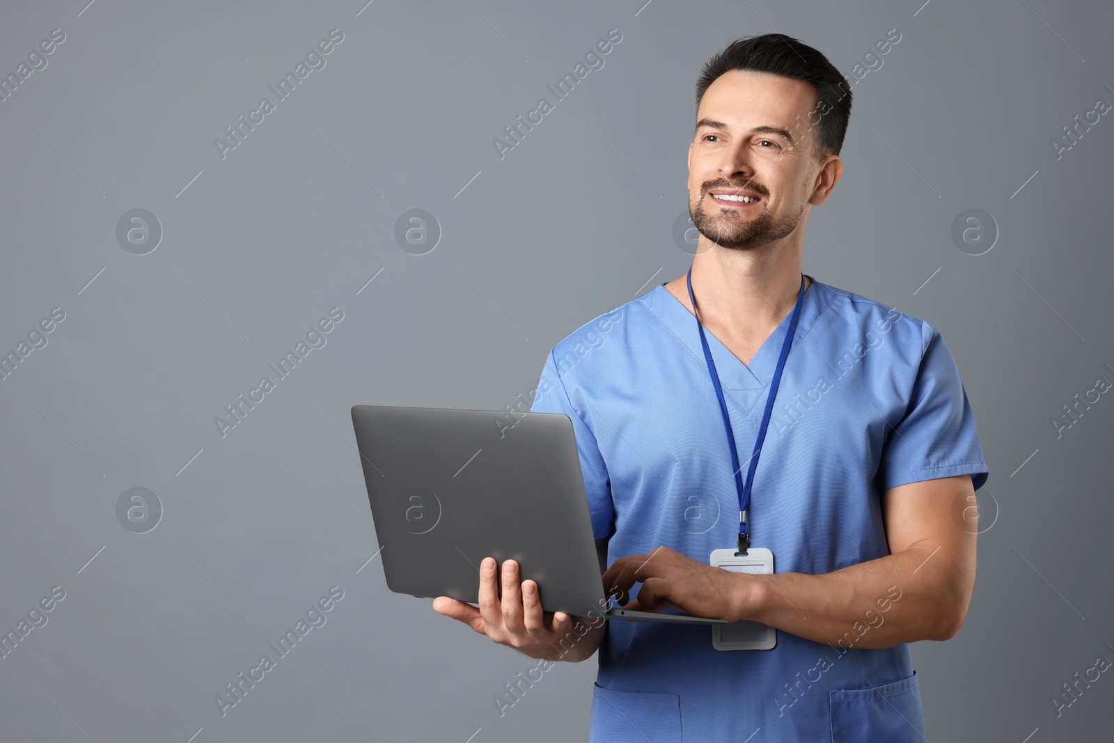 Photo of Smiling nurse with badge and laptop on grey background, space for text