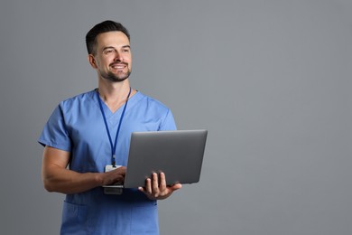 Smiling nurse with badge and laptop on grey background, space for text