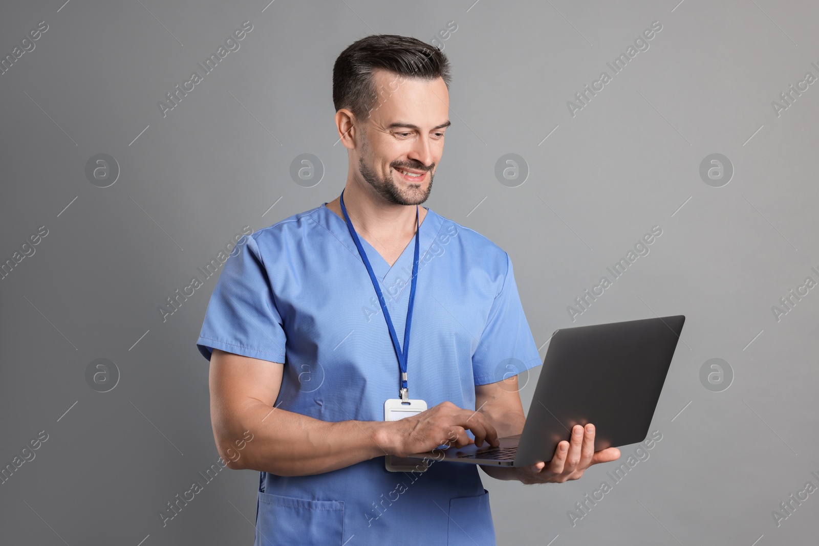 Photo of Smiling nurse with badge using laptop on grey background