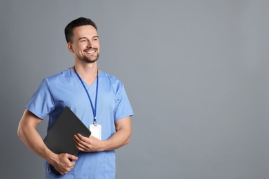 Photo of Smiling nurse with badge and laptop on grey background, space for text