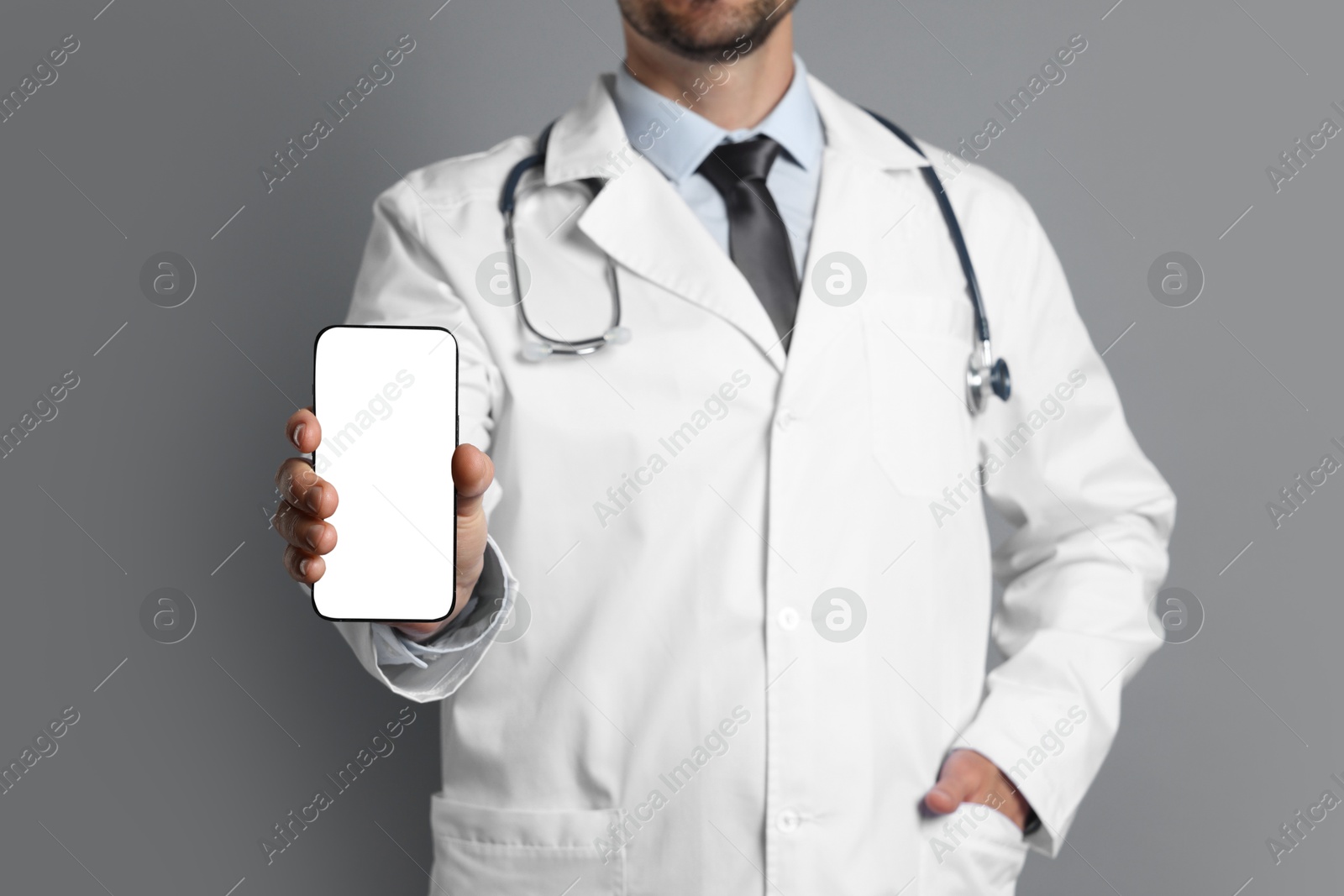 Photo of Doctor showing smartphone with blank screen on grey background, closeup. Mockup for design