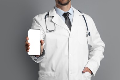 Photo of Doctor showing smartphone with blank screen on grey background, closeup. Mockup for design