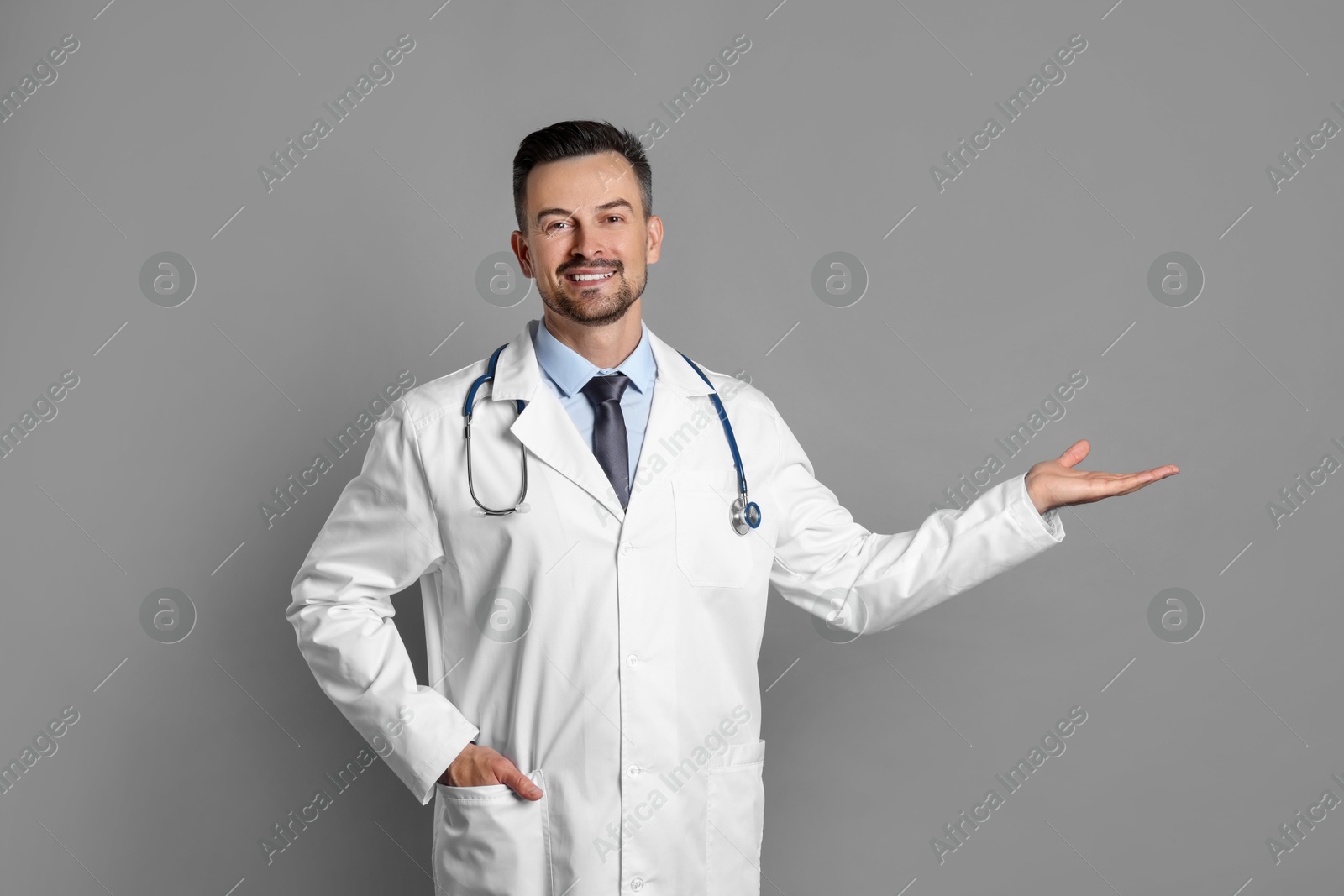 Photo of Smiling doctor with stethoscope pointing at something on grey background