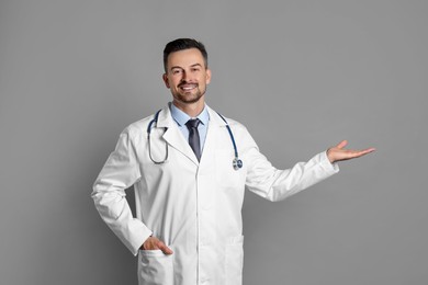 Smiling doctor with stethoscope pointing at something on grey background