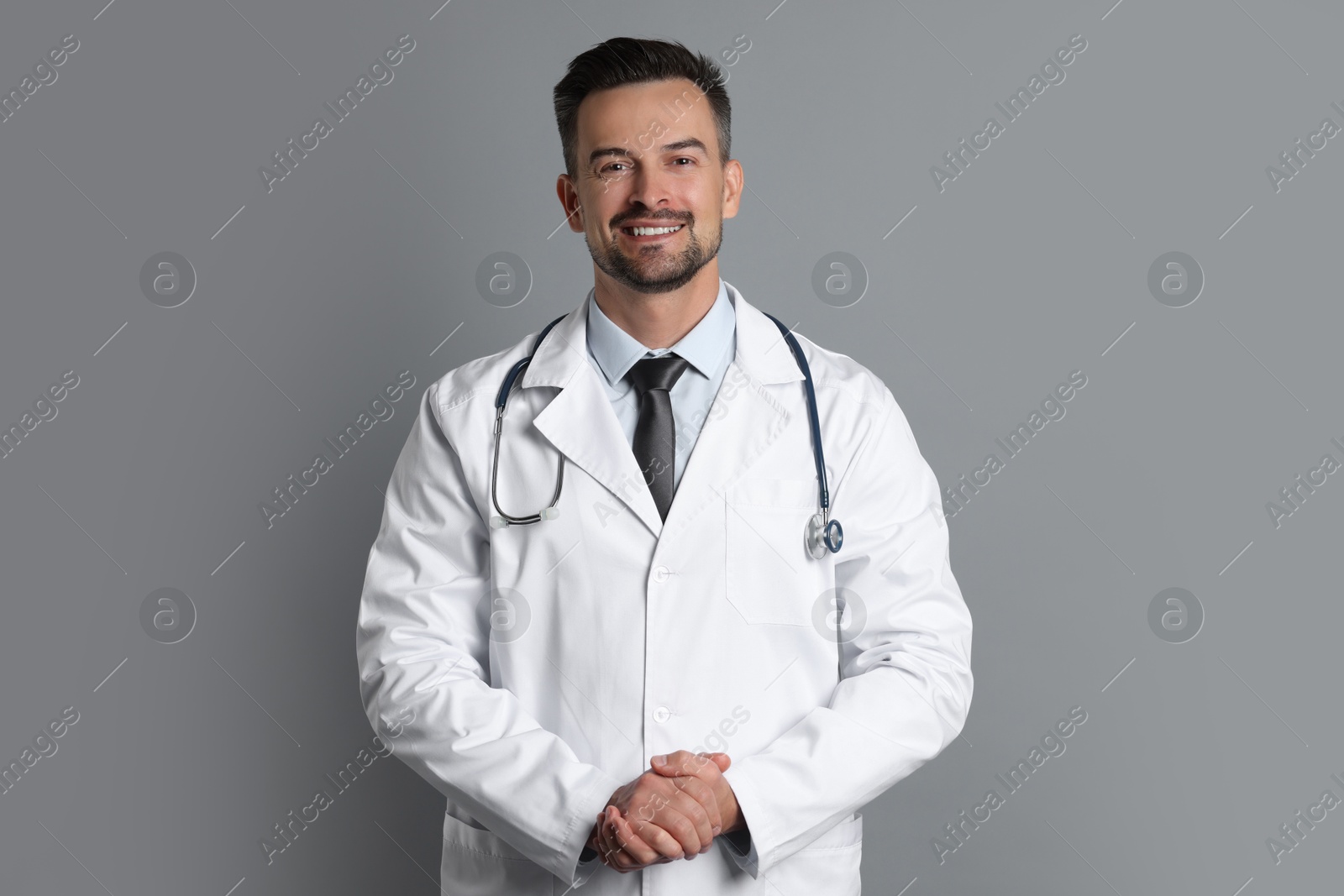 Photo of Smiling doctor with stethoscope on grey background