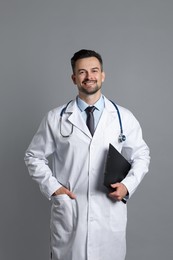 Smiling doctor with stethoscope and clipboard on grey background