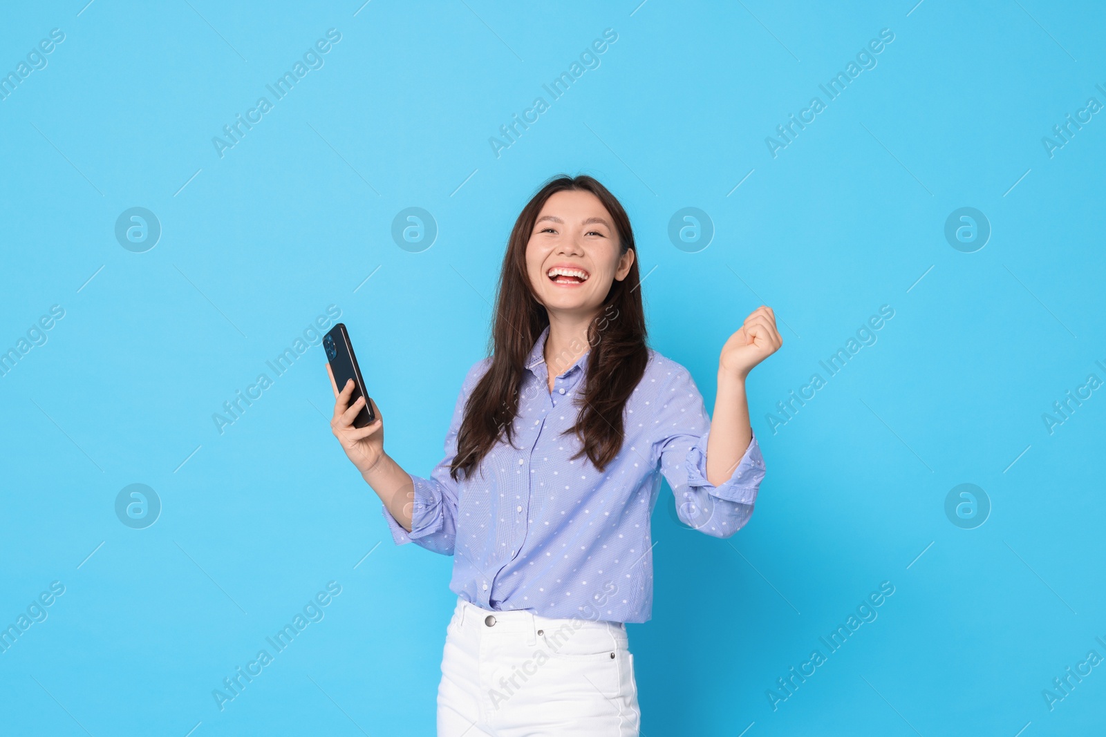 Photo of Smiling woman with smartphone on light blue background