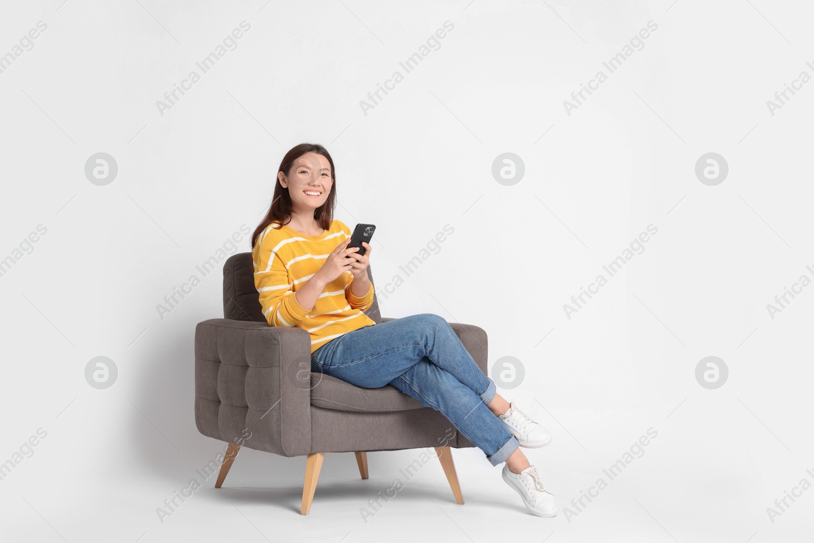 Photo of Smiling woman with smartphone sitting in armchair on white background