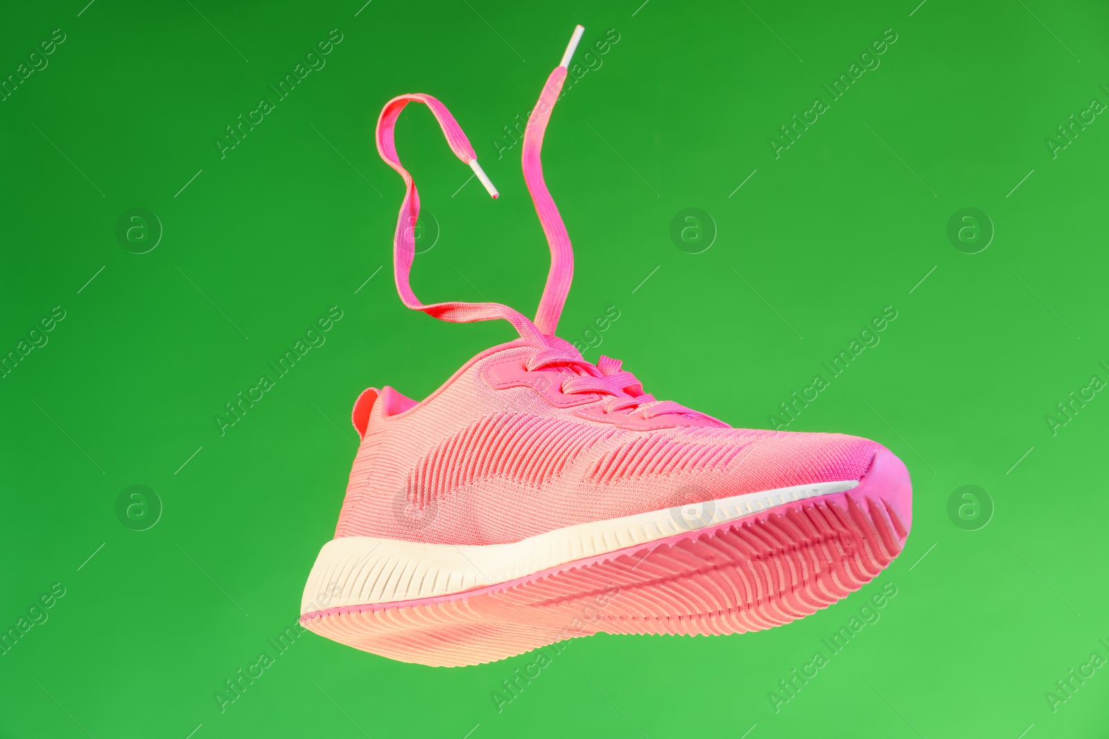 Photo of One stylish pink sneaker in air against green background