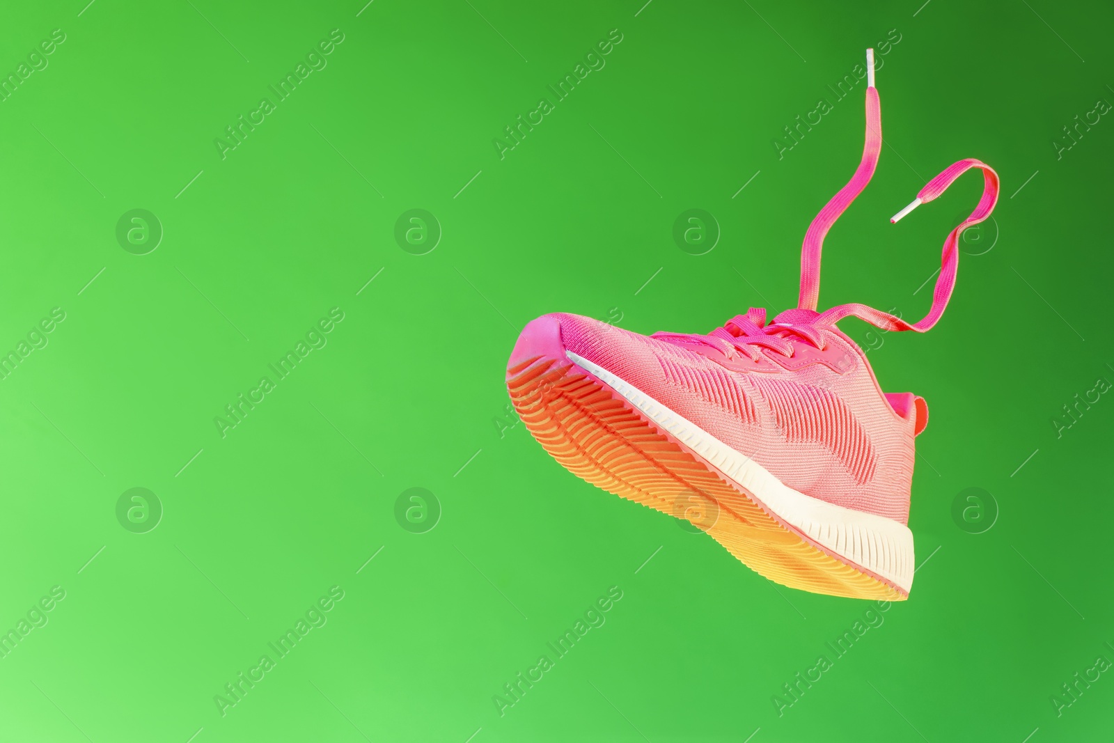 Photo of Stylish sneaker in air against green background, space for text