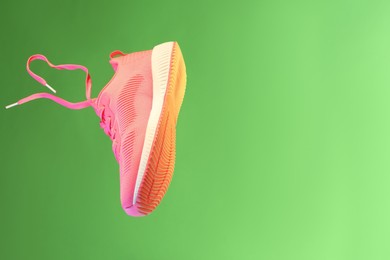 Photo of Stylish sneaker in air against green background, space for text