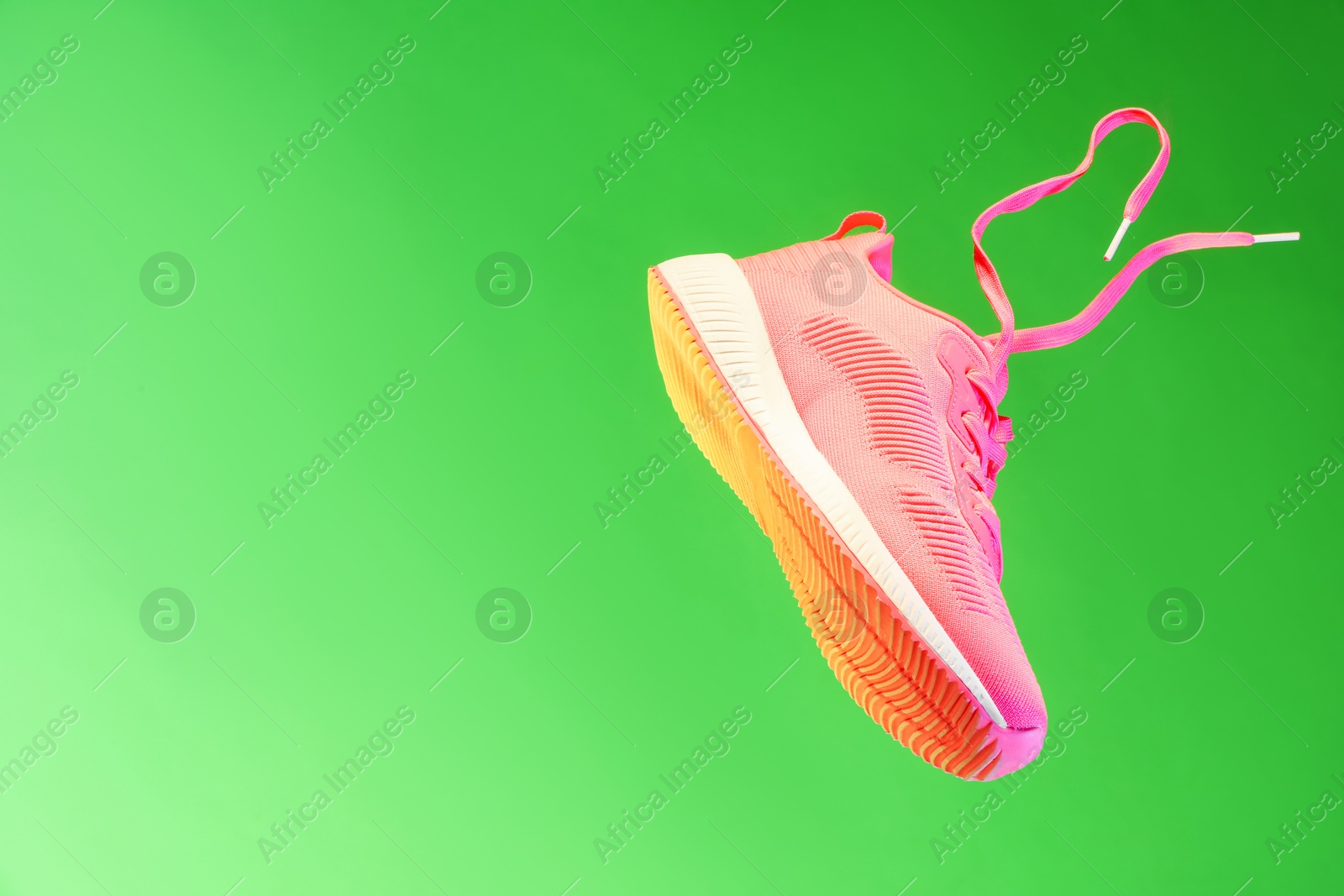 Photo of Stylish sneaker in air against green background, space for text