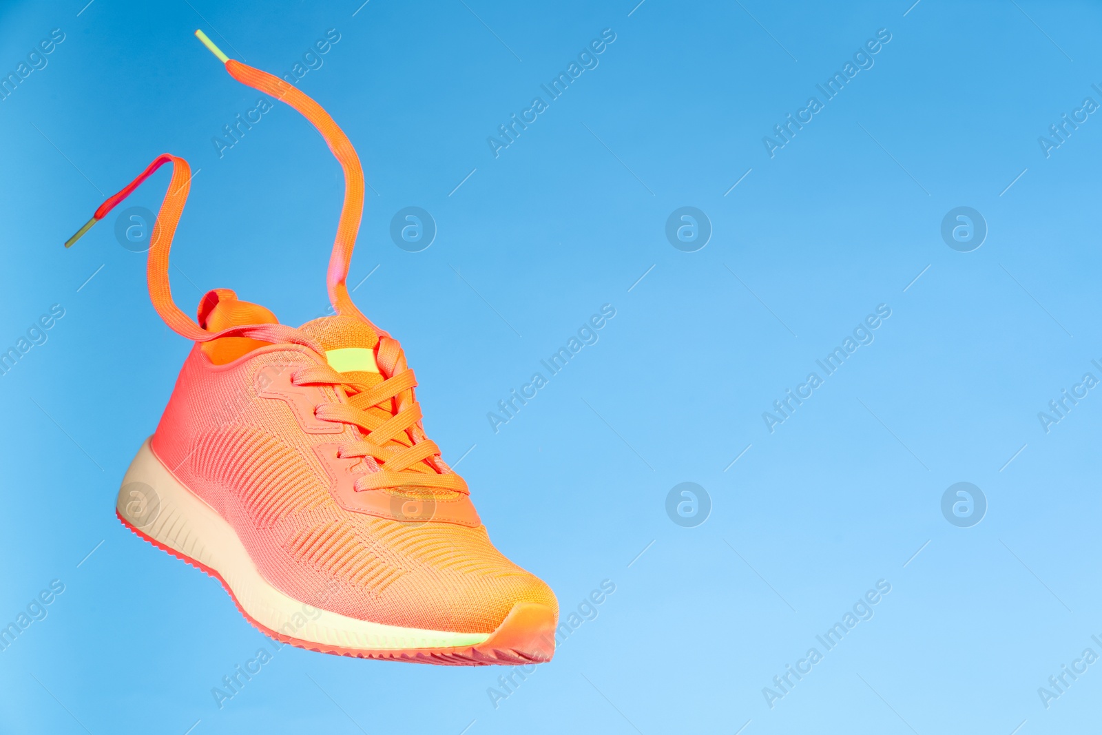 Photo of Stylish sneaker in air against light blue background, space for text