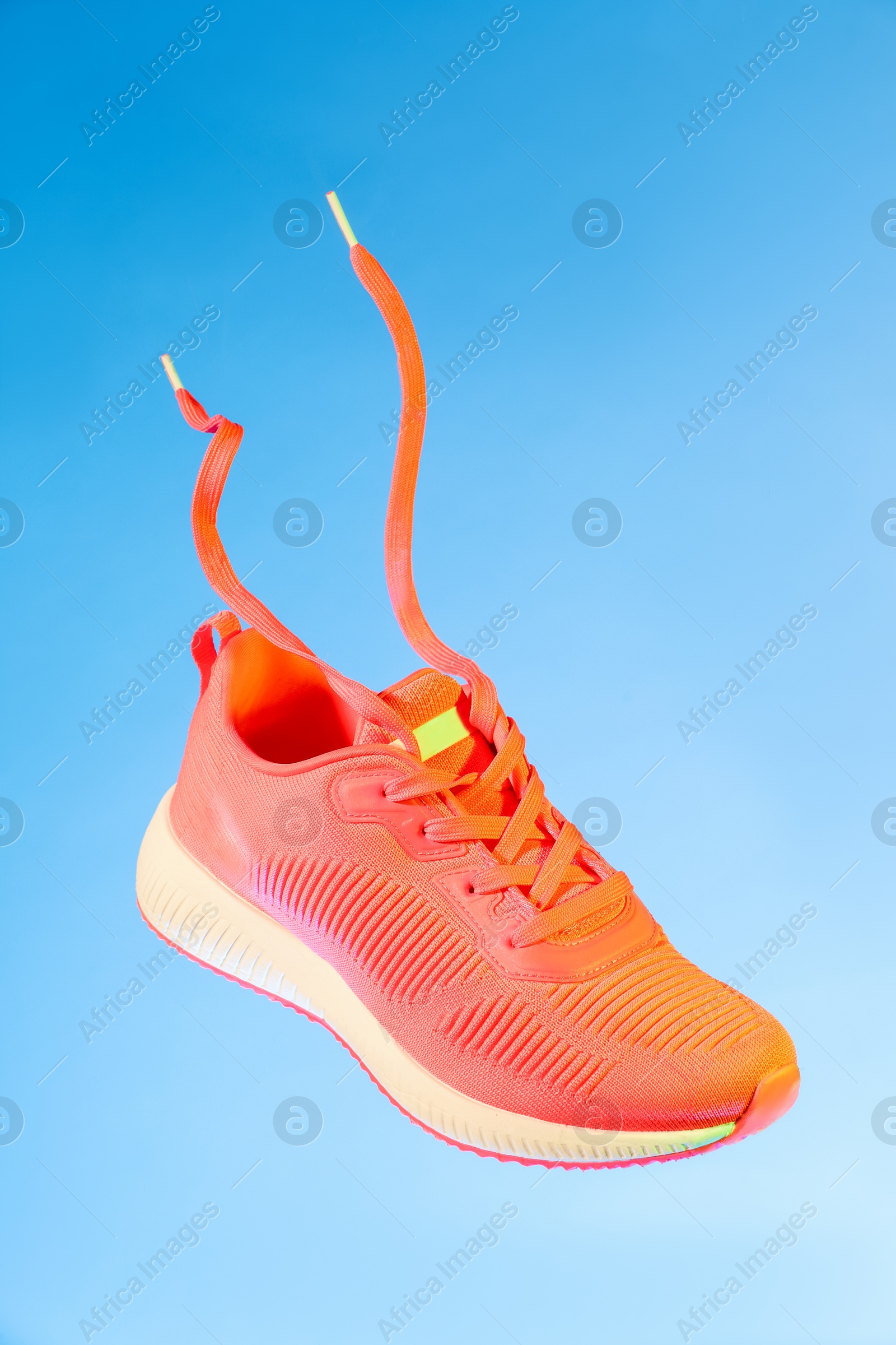 Photo of One stylish bright sneaker in air against light blue background