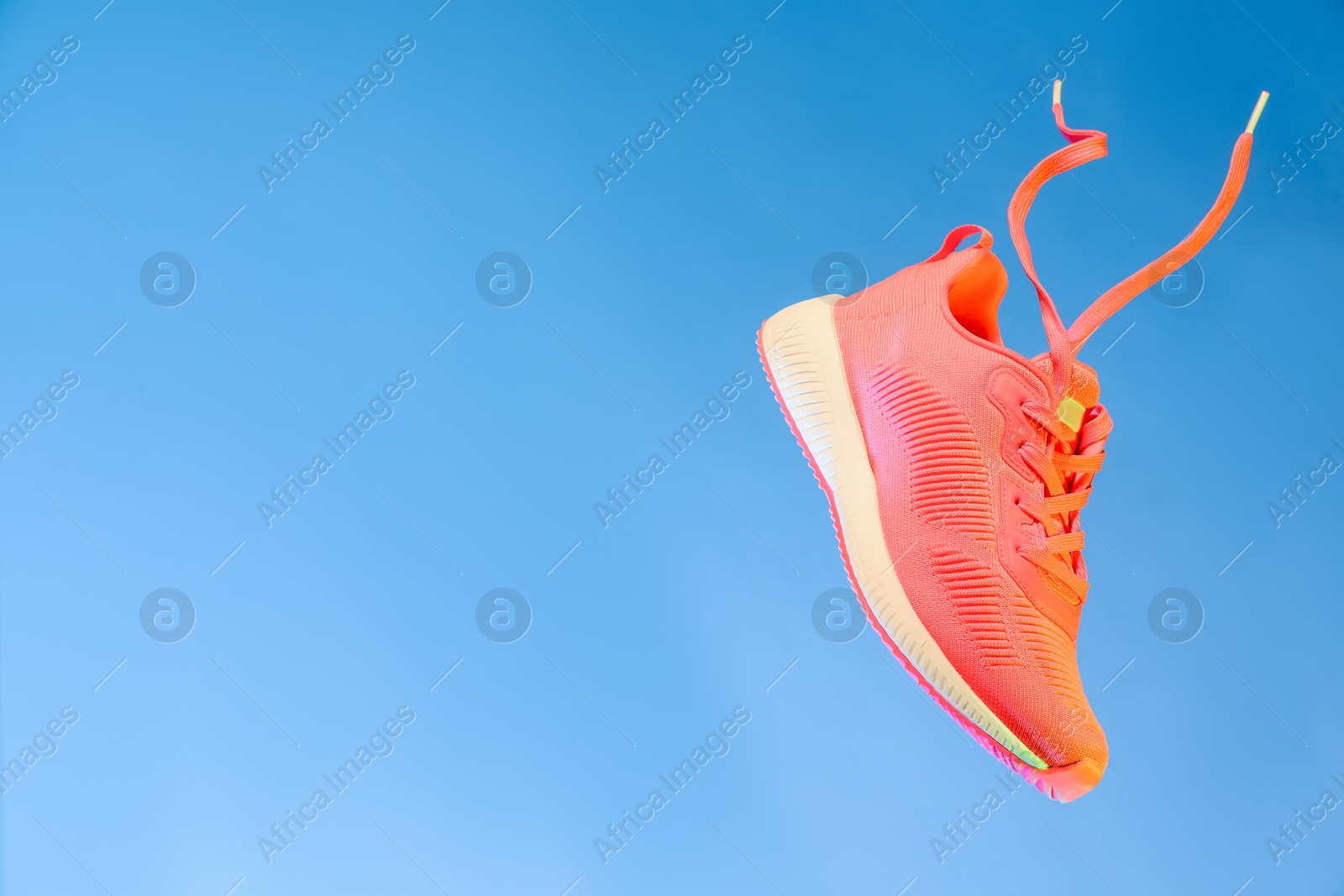 Photo of Stylish sneaker in air against light blue background, space for text