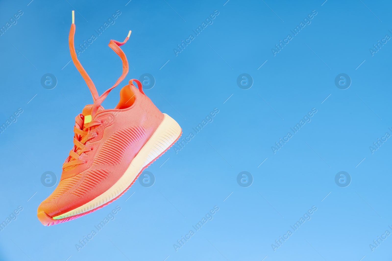 Photo of Stylish sneaker in air against light blue background, space for text