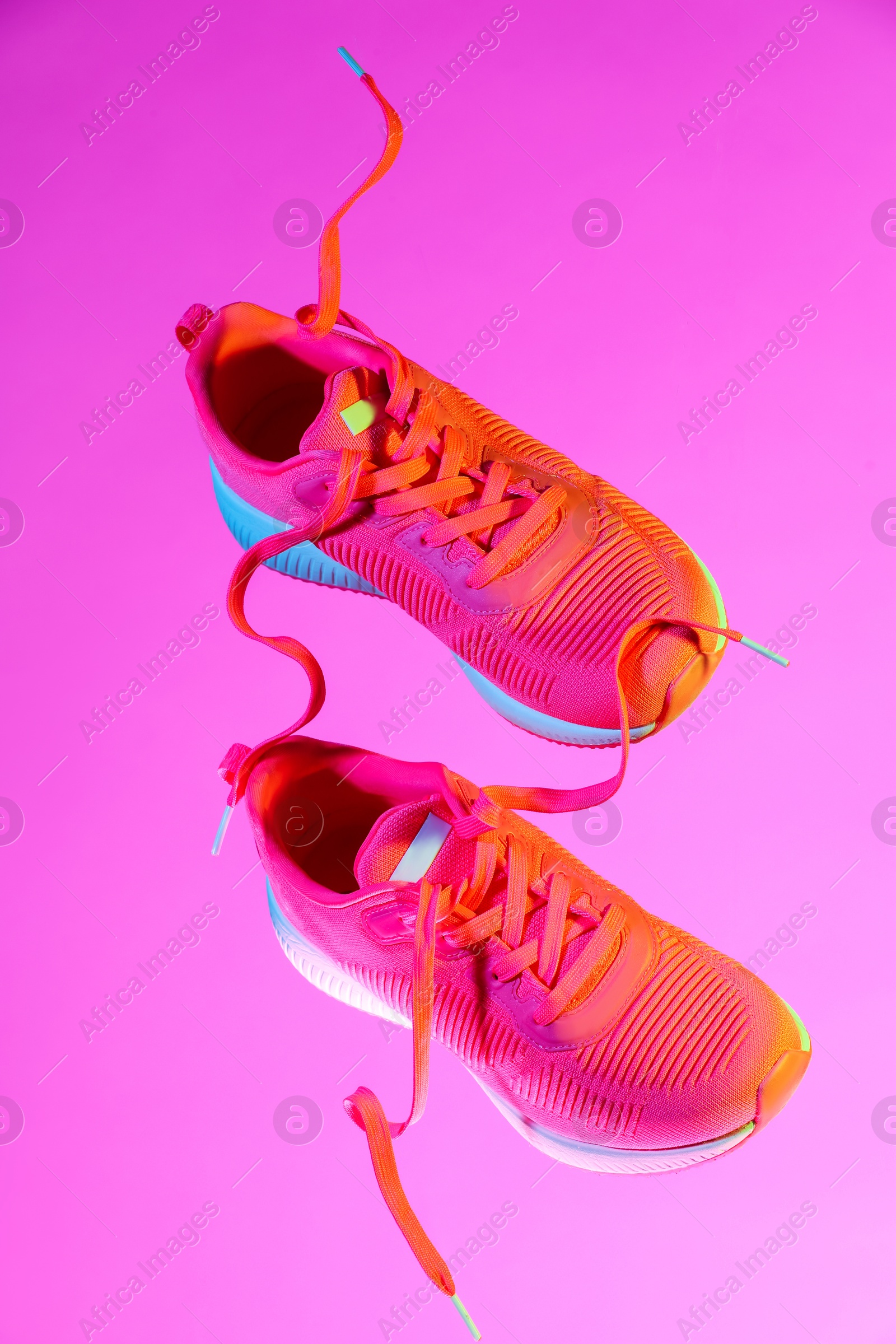 Photo of Pair of stylish sneakers in air against pink background in neon lights