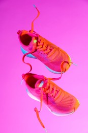 Photo of Pair of stylish sneakers in air against pink background in neon lights