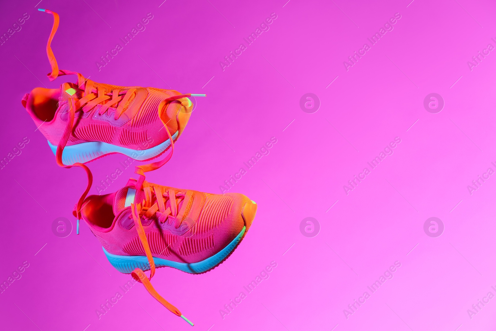 Photo of Pair of stylish sneakers in air against pink background in neon lights, space for text