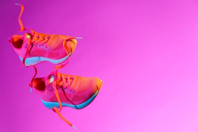 Pair of stylish sneakers in air against pink background in neon lights, space for text