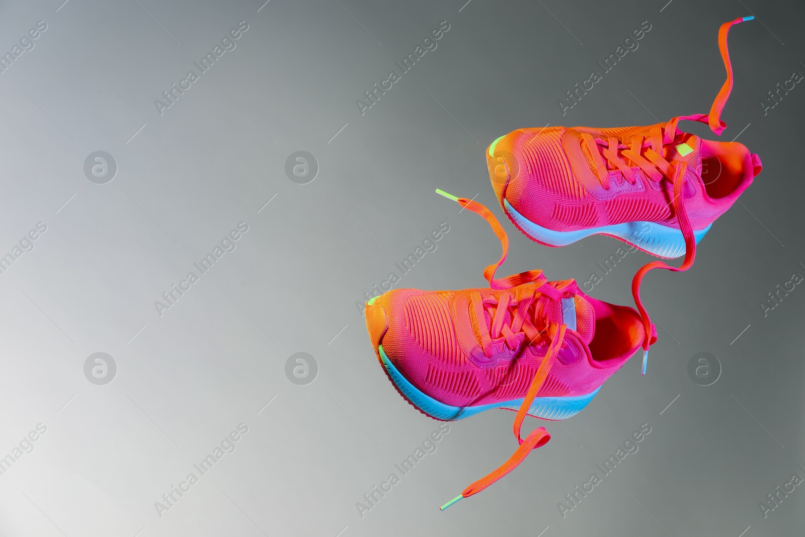 Photo of Pair of stylish sneakers in air against grey background in neon lights, space for text