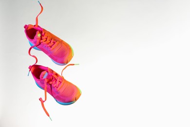 Photo of Pair of stylish sneakers in air against white background in neon lights, space for text