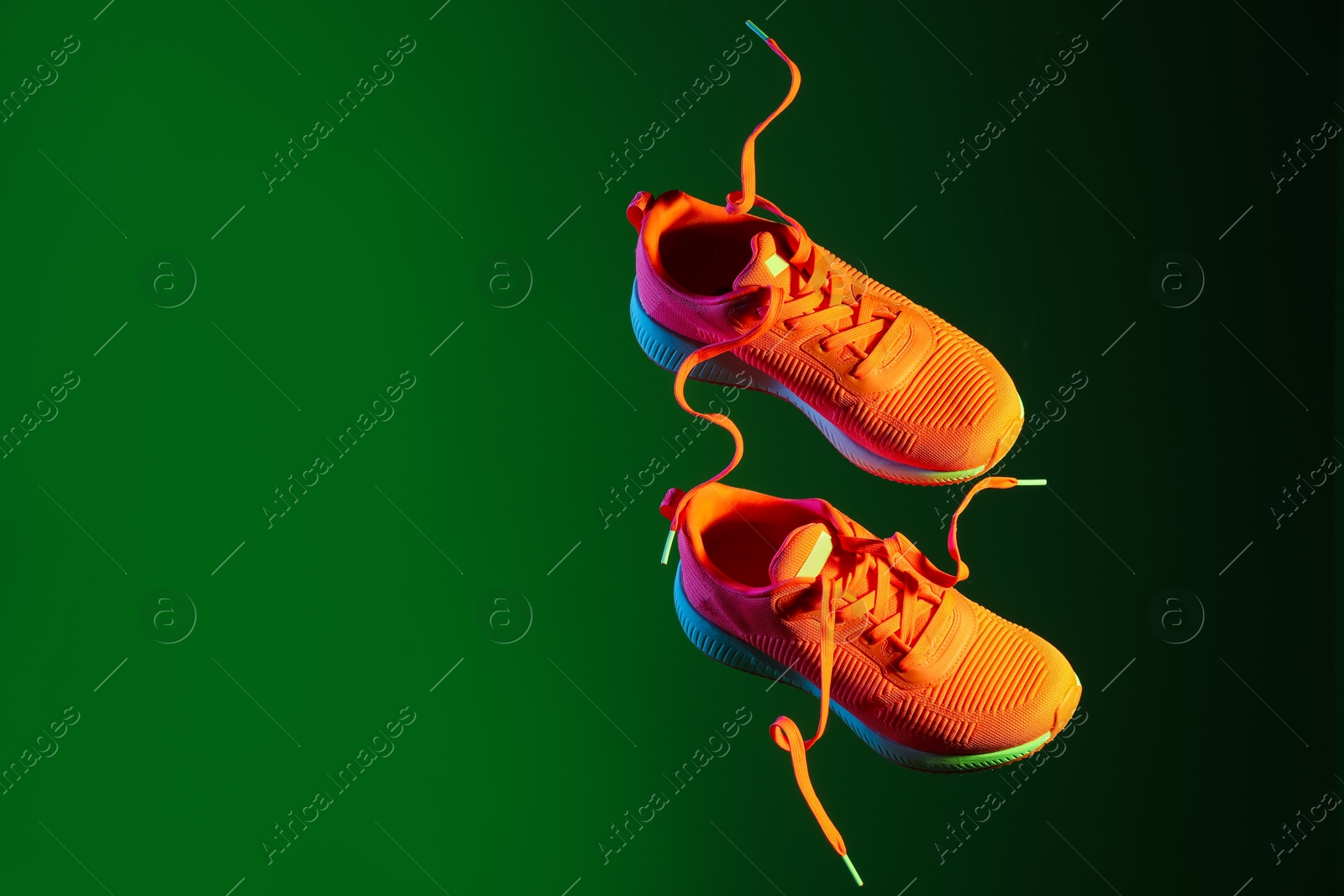 Photo of Pair of stylish sneakers in air against dark green background, space for text