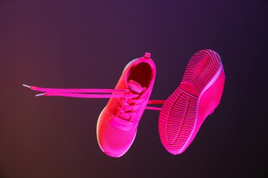 Photo of Pair of stylish sneakers in air against dark purple background