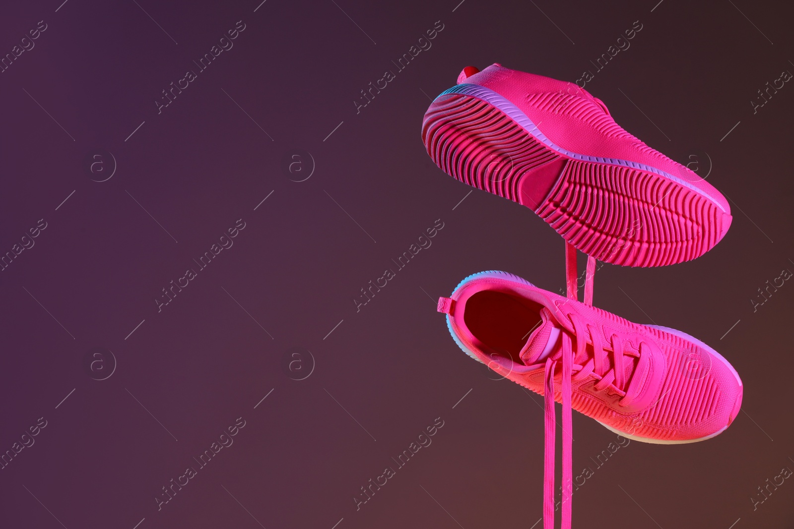 Photo of Pair of stylish sneakers in air against dark purple background, space for text