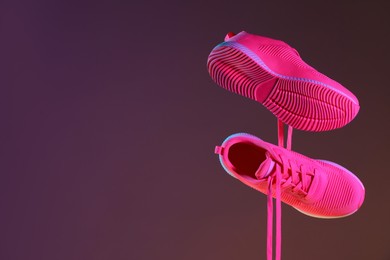 Photo of Pair of stylish sneakers in air against dark purple background, space for text