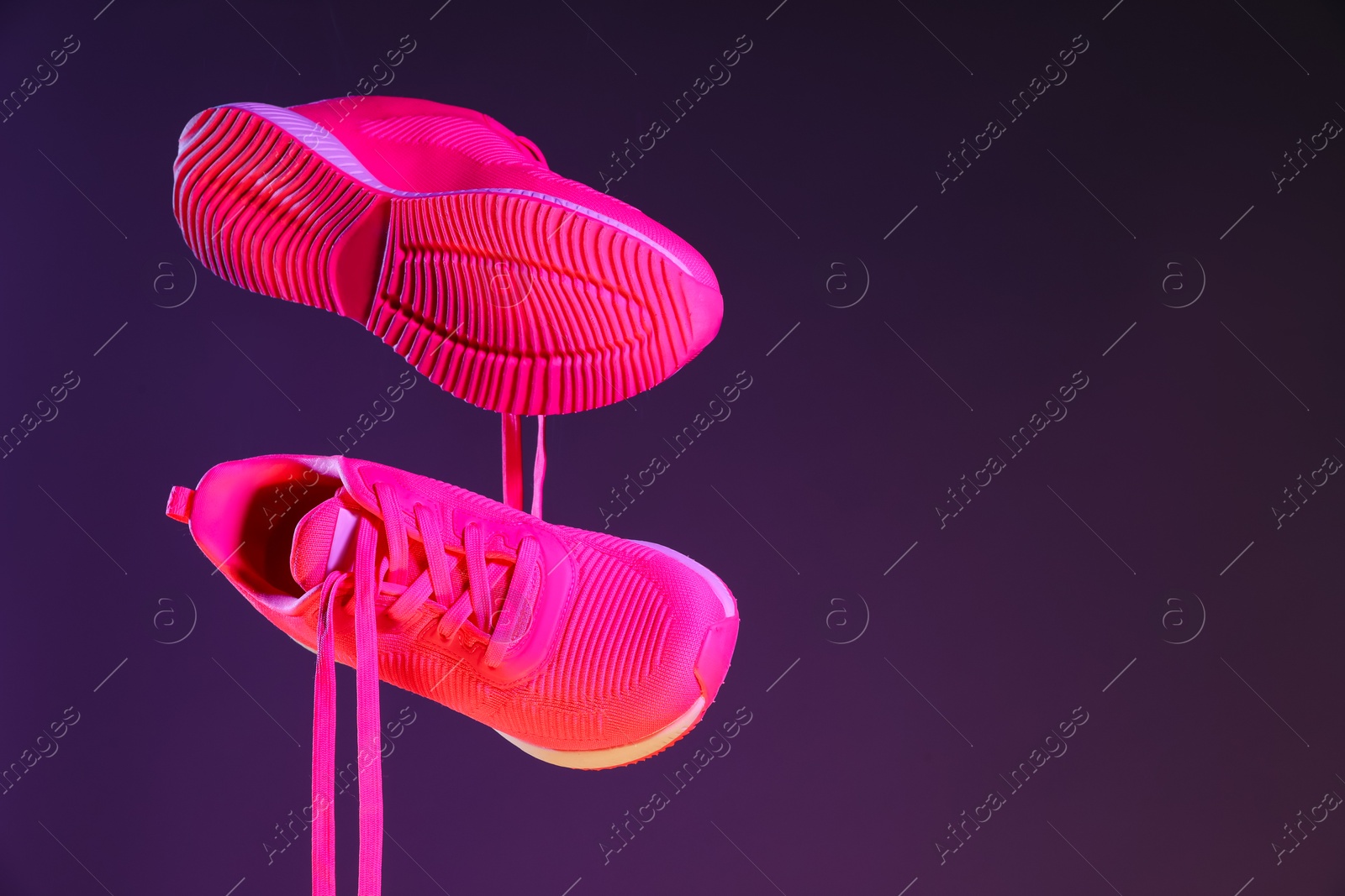 Photo of Pair of stylish sneakers in air against dark purple background, space for text