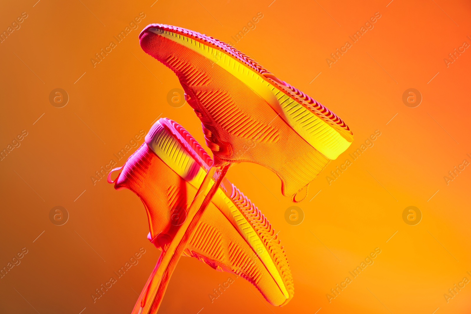 Photo of Pair of stylish sneakers in air against bright background in neon lights