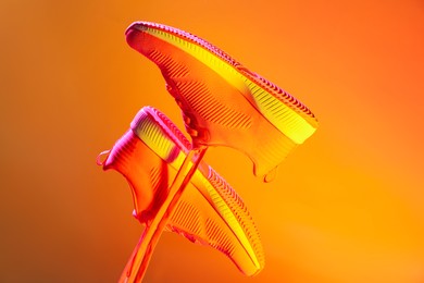 Photo of Pair of stylish sneakers in air against bright background in neon lights