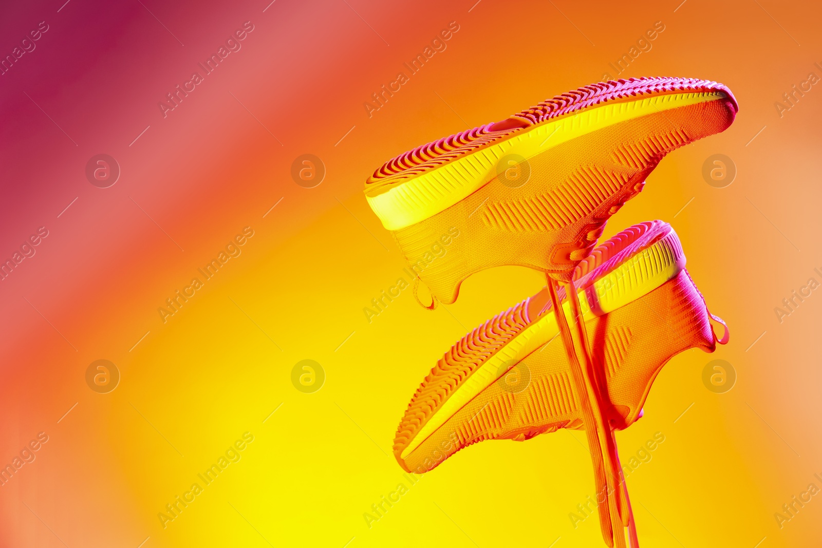 Photo of Pair of stylish sneakers in air against bright background in neon lights, space for text