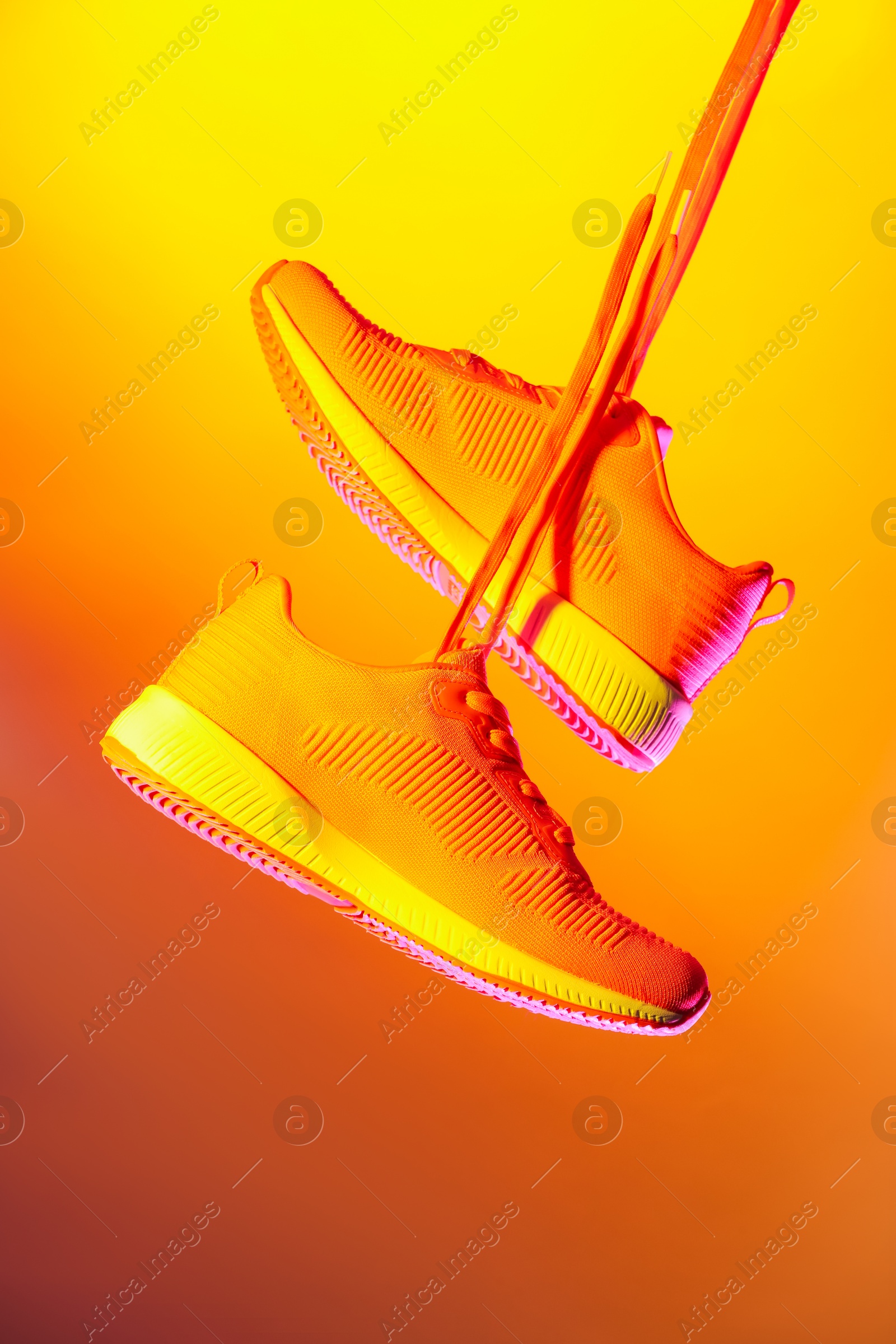 Photo of Pair of stylish sneakers in air against bright background in neon lights