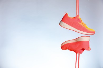 Photo of Pair of stylish sneakers in air against light grey background in neon lights, space for text