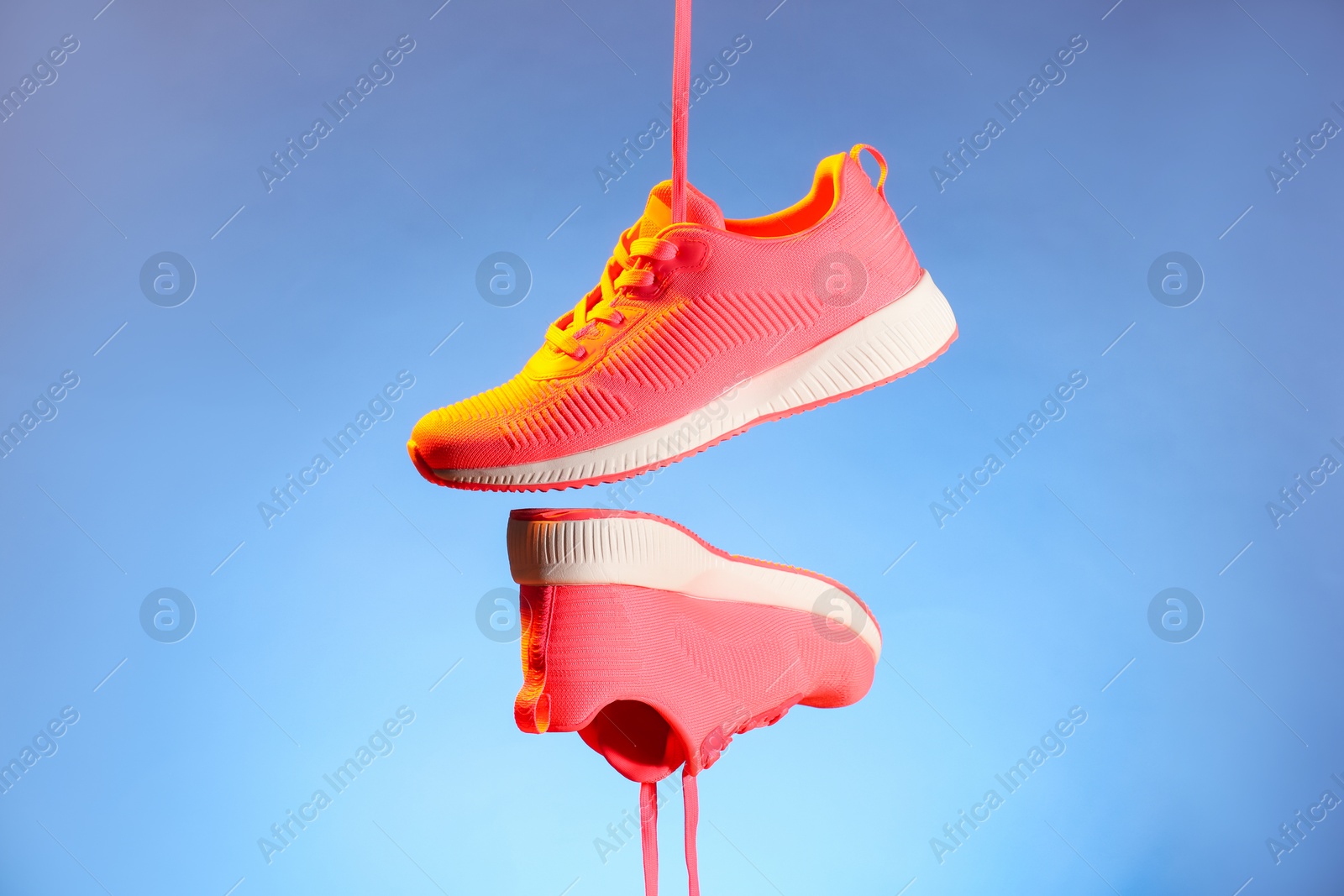 Photo of Pair of stylish sneakers in air against light blue background in neon lights