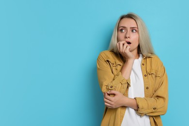 Portrait of scared woman on light blue background, space for text