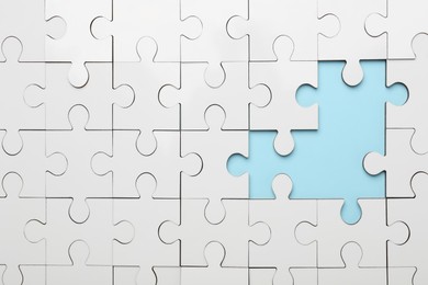 Photo of White puzzle with missing pieces on light blue background, top view