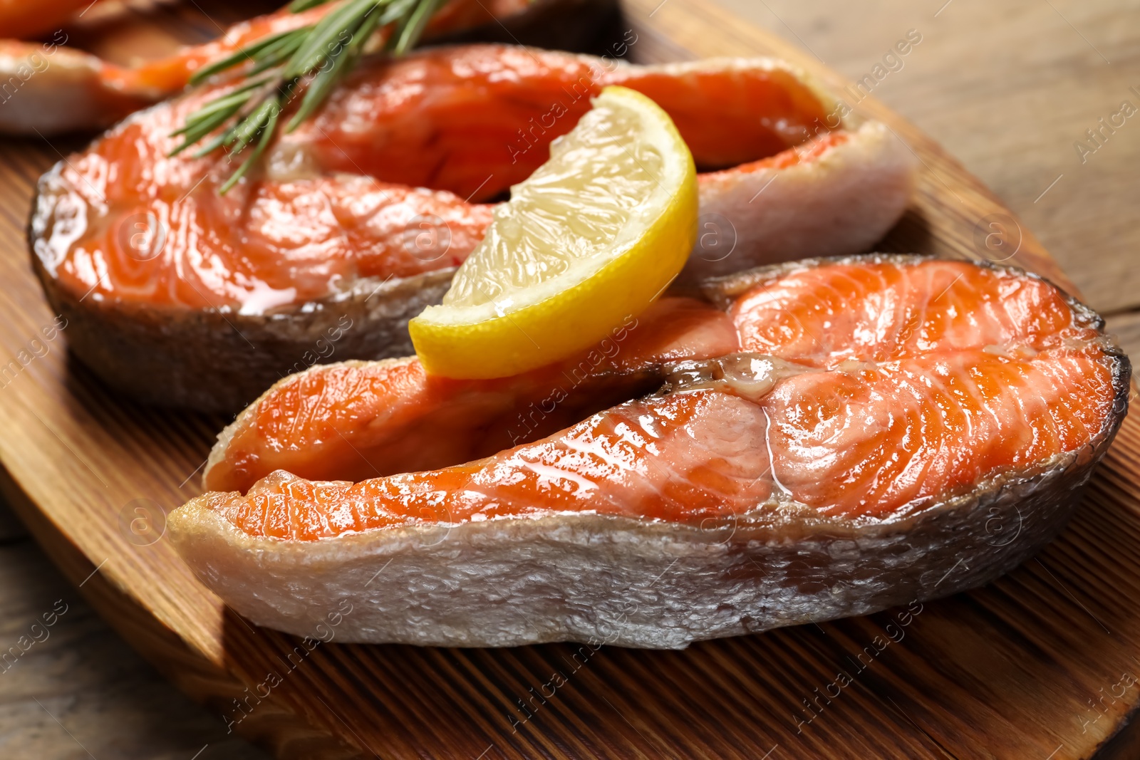 Photo of Tasty grilled salmon steaks, lemon and rosemary on wooden table, closeup