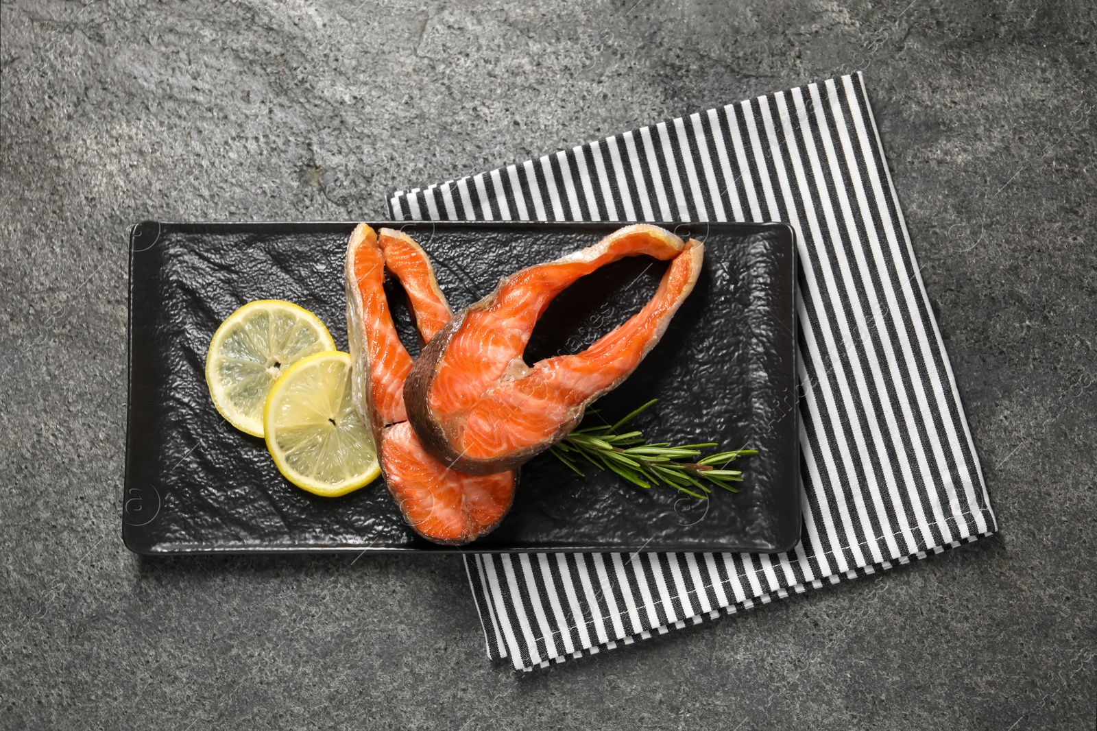 Photo of Tasty grilled salmon steaks, lemon and rosemary on gray textured table, top view