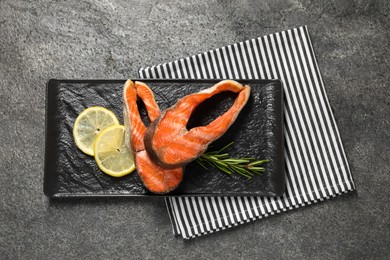 Photo of Tasty grilled salmon steaks, lemon and rosemary on gray textured table, top view