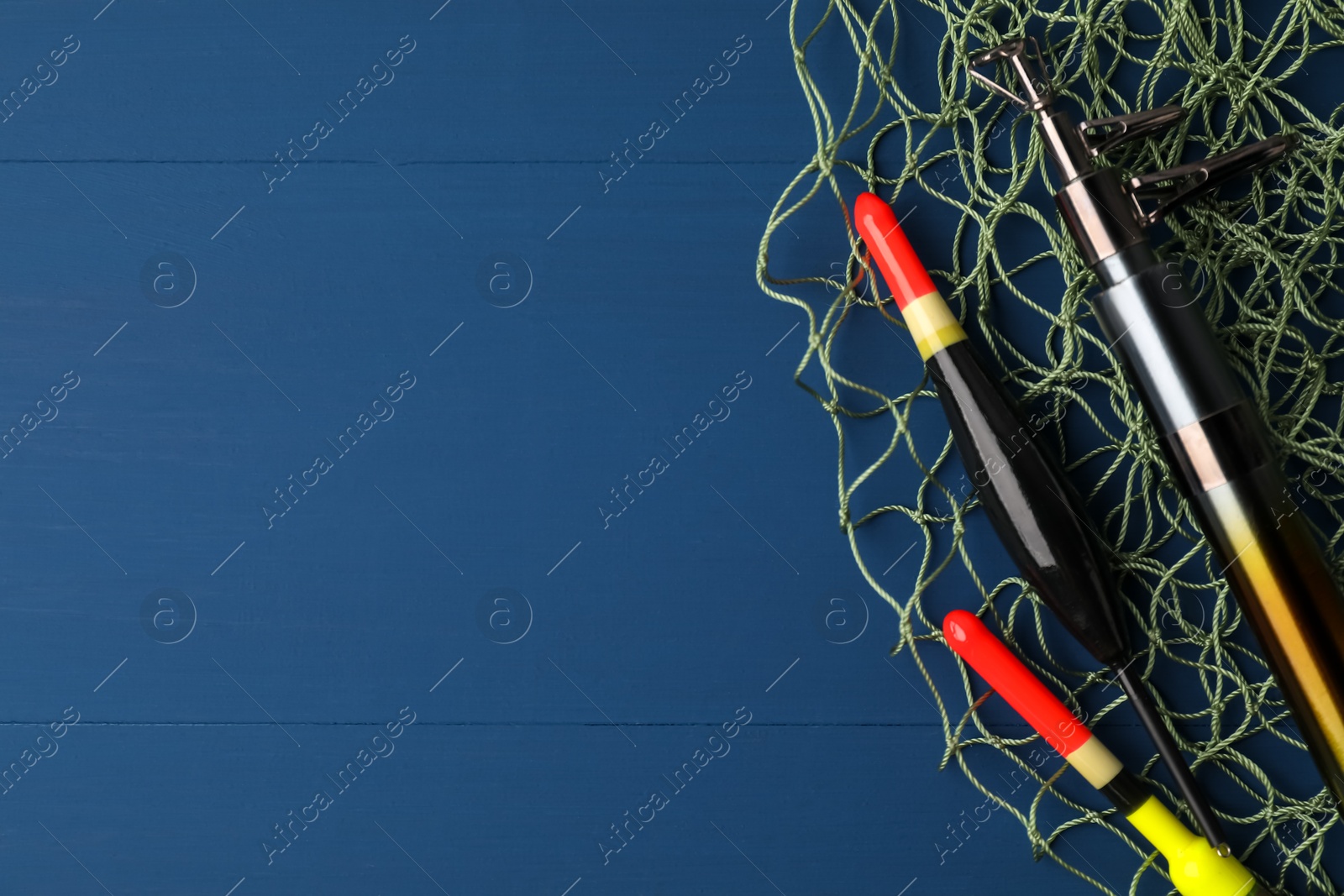 Photo of Fishing rod, floats and net on blue wooden table, top view. Space for text