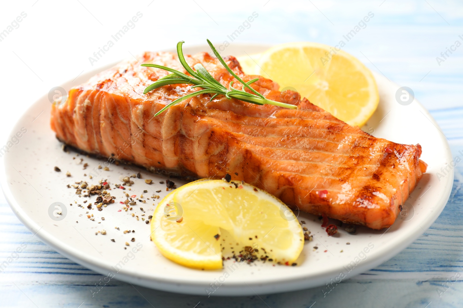 Photo of Delicious grilled salmon fillet served on light blue wooden table, closeup