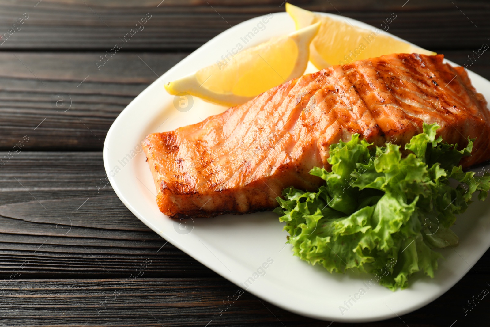 Photo of Delicious grilled salmon fillet served on wooden table, closeup