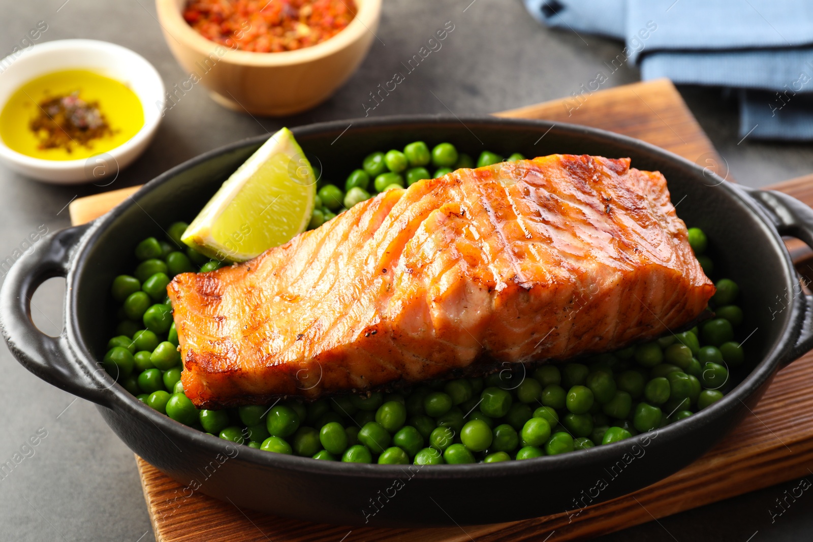 Photo of Delicious grilled salmon fillet with green peas and lime in baking dish on grey table, closeup