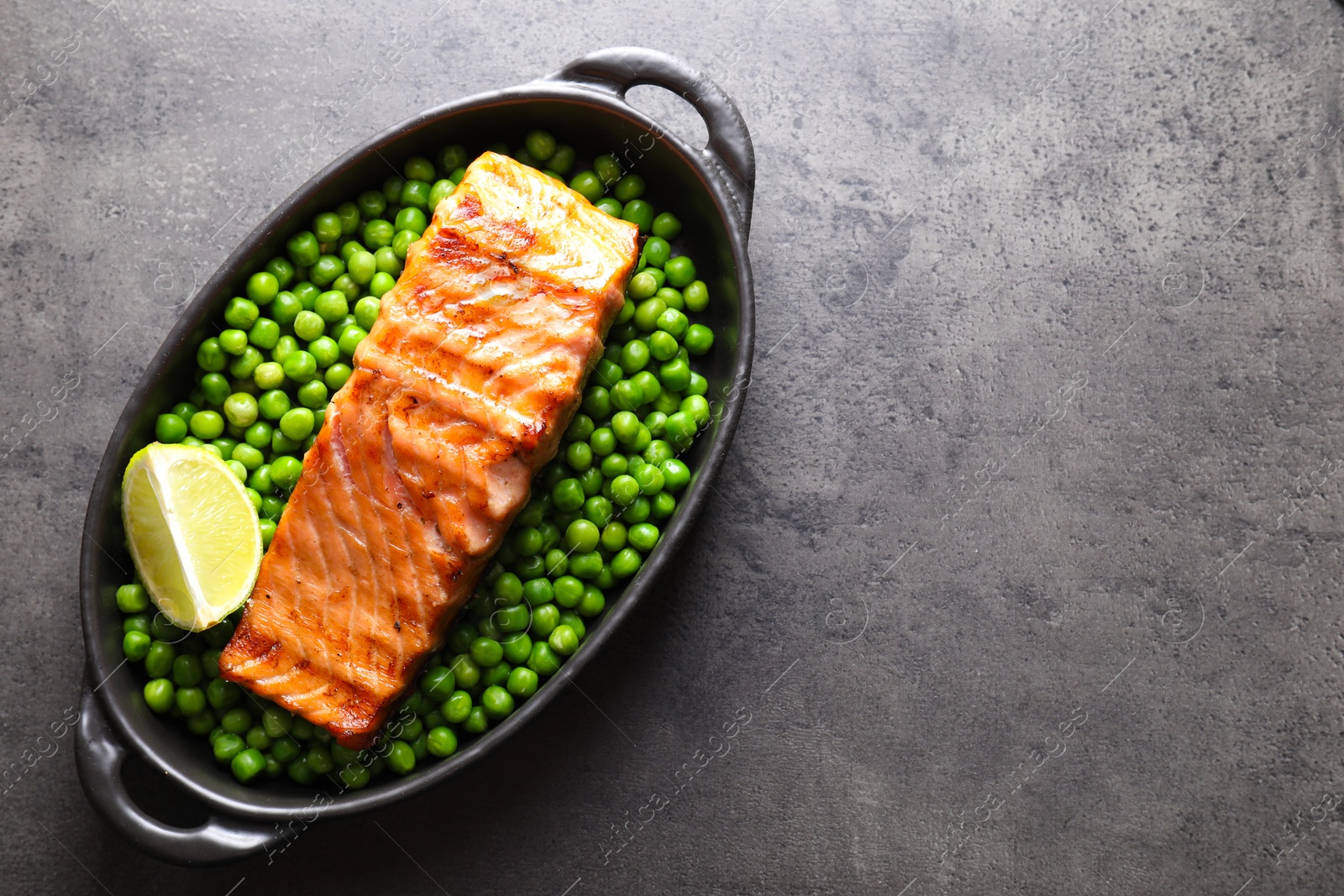 Photo of Delicious grilled salmon fillet with green peas and lime in baking dish on grey textured table, top view. Space for text