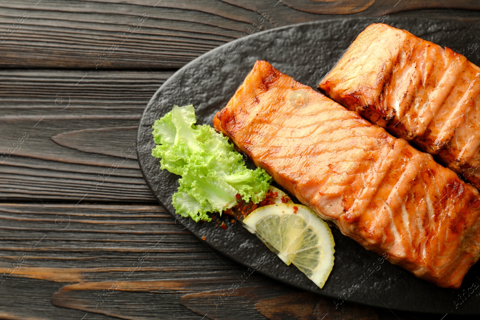 Photo of Delicious grilled salmon fillets with lettuce and lemon on wooden table, top view. Space for text