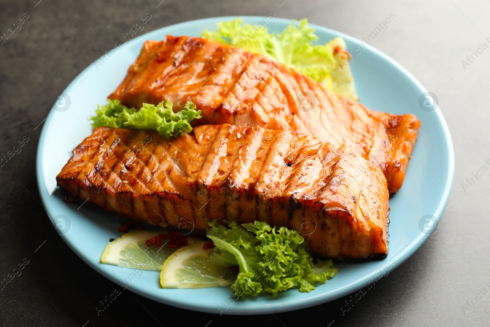 Photo of Delicious grilled salmon fillets with lettuce and lemon on grey table, closeup