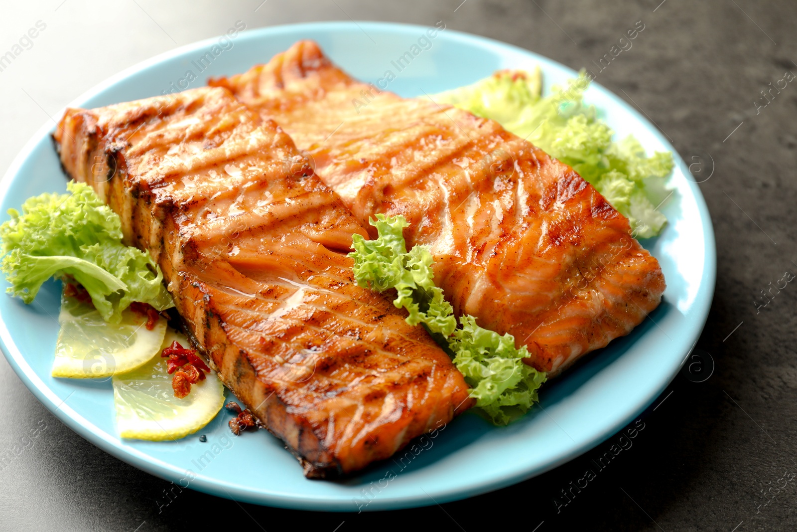 Photo of Delicious grilled salmon fillets with lettuce and lemon on grey table, closeup